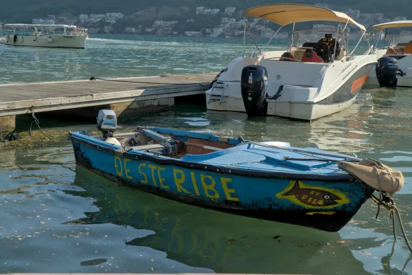 Old blue fishing boat with yellow lettering "DE STERIBE" and fish symbol, floating in the Bay of Kotor next to a pier and modern boats.