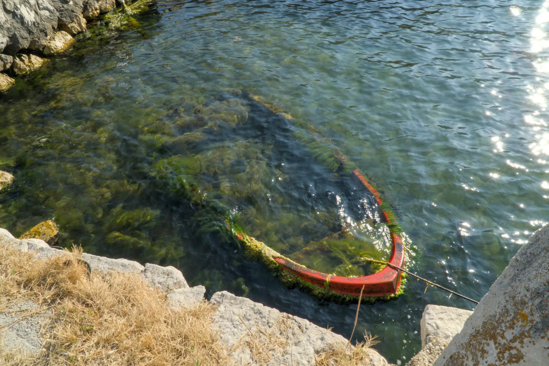 Die Kante eines alten, roten, versunkenen Bootes, bedeckt mit Algen, treibt im ruhigen Wasser der Bucht von Kotor.