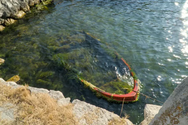 The edge of an old, red, sunken boat, covered in algae, floats in the calm waters of the Bay of Kotor.