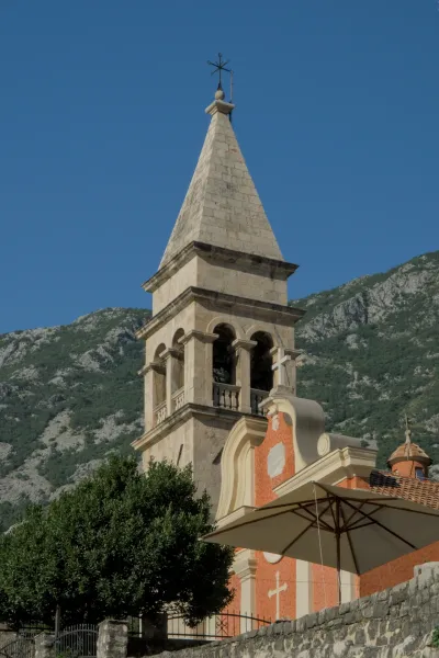 Bell tower of the Church of Saint Matthew in Dobrota, Montenegro with rocky mountains in the background.