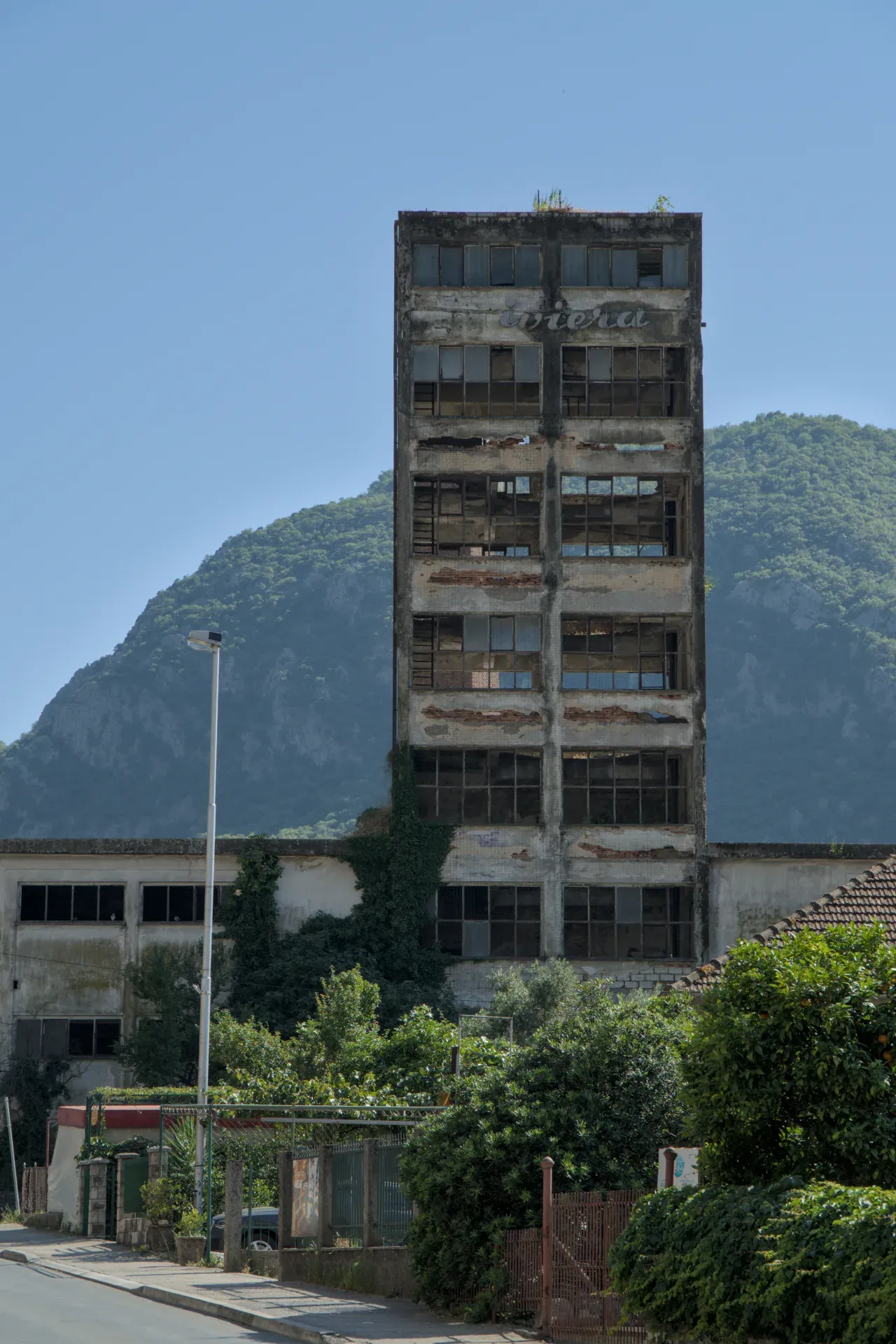 Ein verfallenes, mehrstöckiges Gebäude in Kotor, Montenegro, mit Fenstern und bergiger Landschaft im Hintergrund.