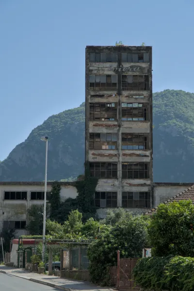 A decaying, multi-story building in Kotor, Montenegro, featuring windows and a mountainous landscape in the background.