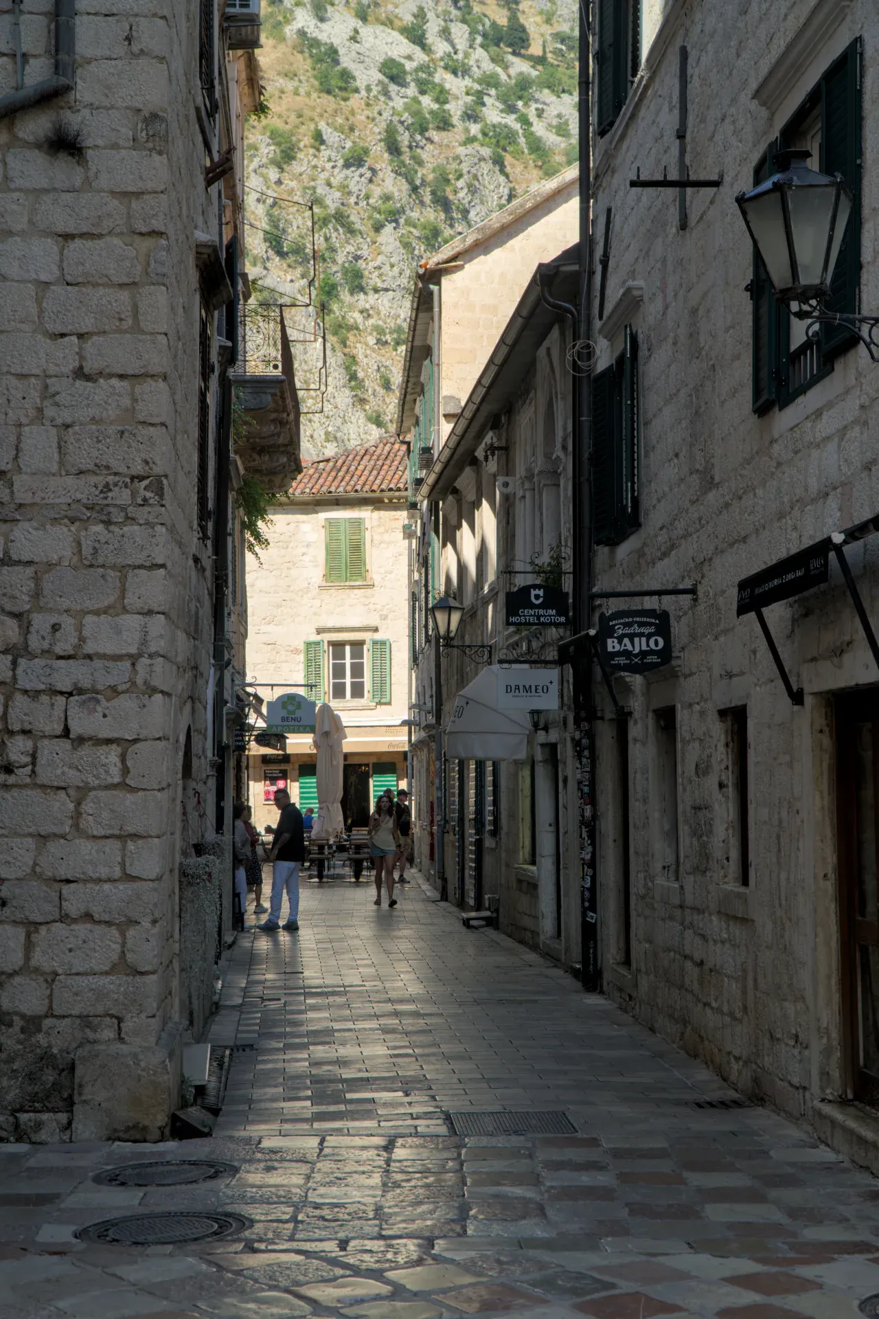 Vicolo soleggiato nel centro storico di Kotor, Montenegro, con edifici in pietra e vista sulle montagne.
