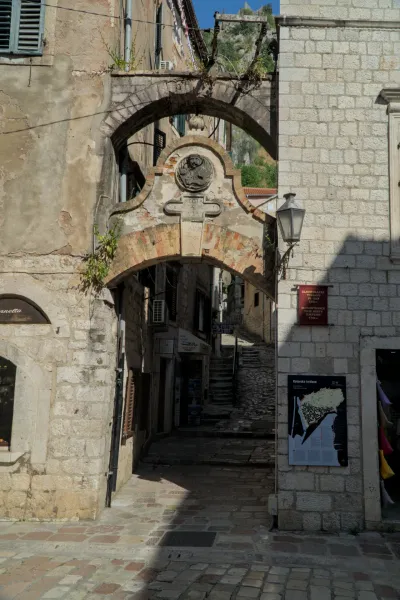 An old stone archway passage in Kotor, Montenegro, with shadows and light on the cobblestones and buildings.
