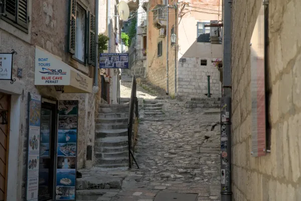 A steep, cobblestone alley in Kotor, Montenegro, with stone buildings and a stone staircase leading upwards.