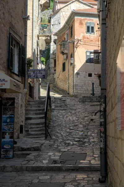 A steep, cobblestone alley in Kotor, Montenegro, lined with historic buildings and stone stairs, with dramatic light.