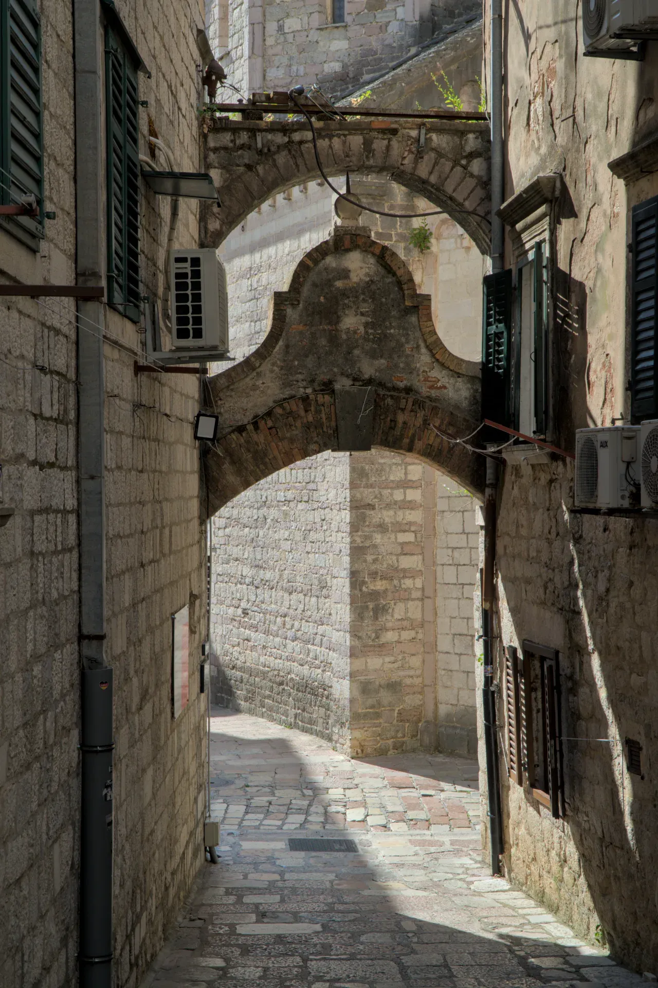 Stari kameni lukovi u uskoj ulici u Kotoru, Crna Gora, sa suncem i senkama.