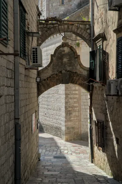 Old stone archways in a narrow alley in Kotor, Montenegro, with sunshine and shadows.