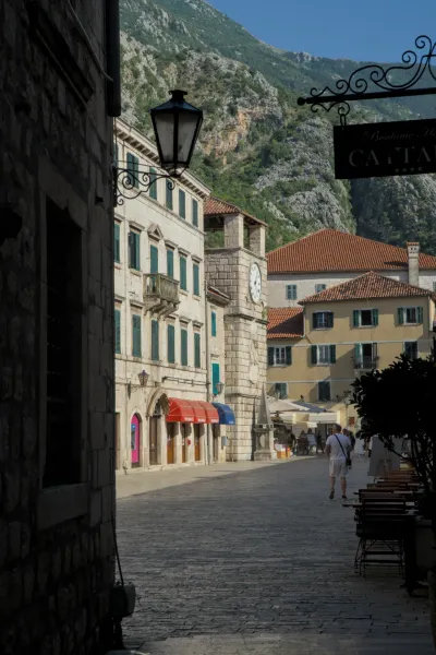 Painterly shot of an alley in Kotor with a historic clock tower, framed by old buildings and mountain landscape.