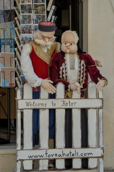 Traditionally dressed figures greet visitors in front of a "Welcome to Kotor" sign in Montenegro.