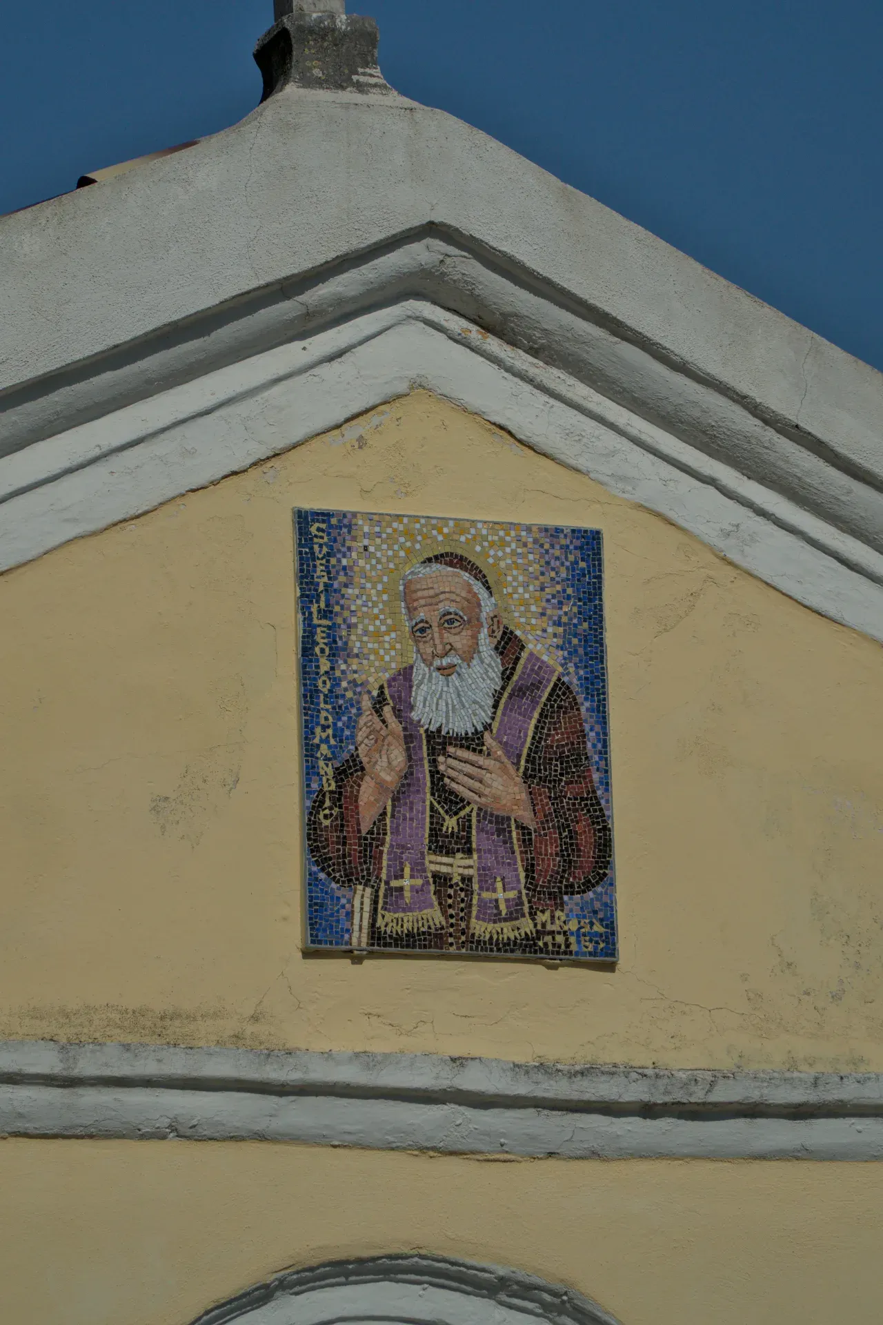 Mosaico dettagliato di un santo barbuto con veste viola su una facciata gialla a Herceg Novi, Montenegro.