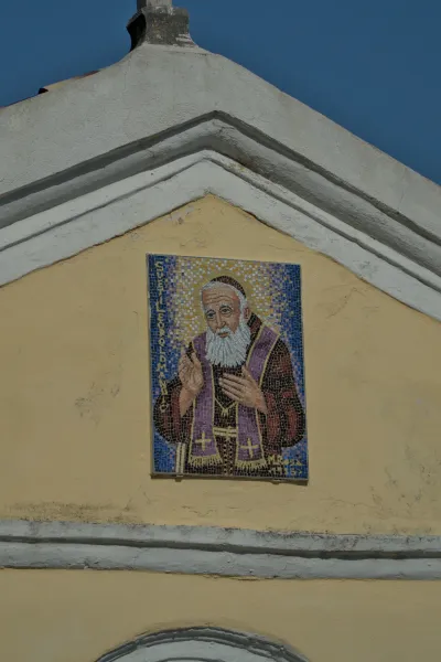 Detailed mosaic of a bearded saint in purple robes on a yellow facade in Herceg Novi, Montenegro.