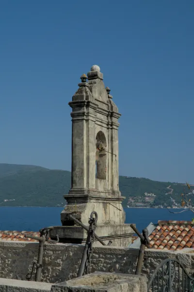 A stone clock tower stands out against a deep blue sky and the sea, with historic anchors in the foreground.