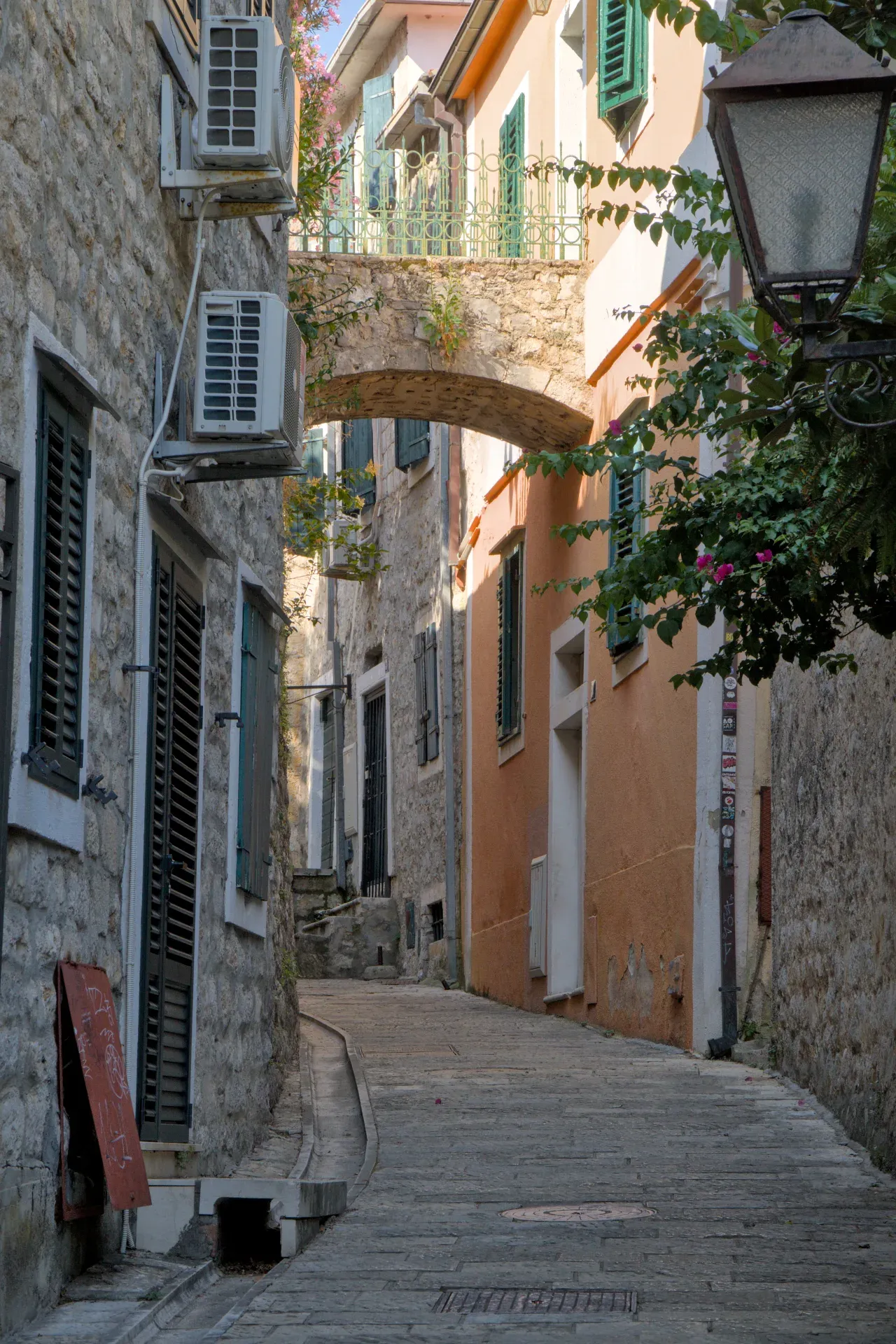 A narrow, stone alley in Herceg Novi under a stone arch with warm-toned buildings.