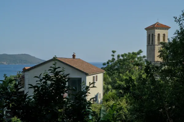A traditional Mediterranean house with a tiled roof and sea view, next to a prominent church tower in Herceg Novi, Montenegro.