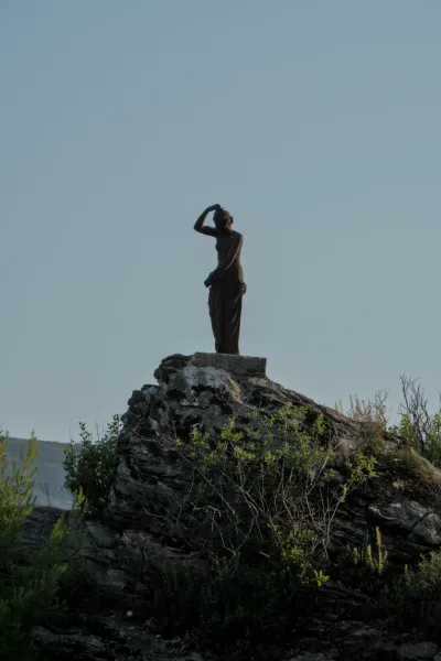 Bronze statue of a woman on a rocky outcrop against a clear sky in Herceg Novi.