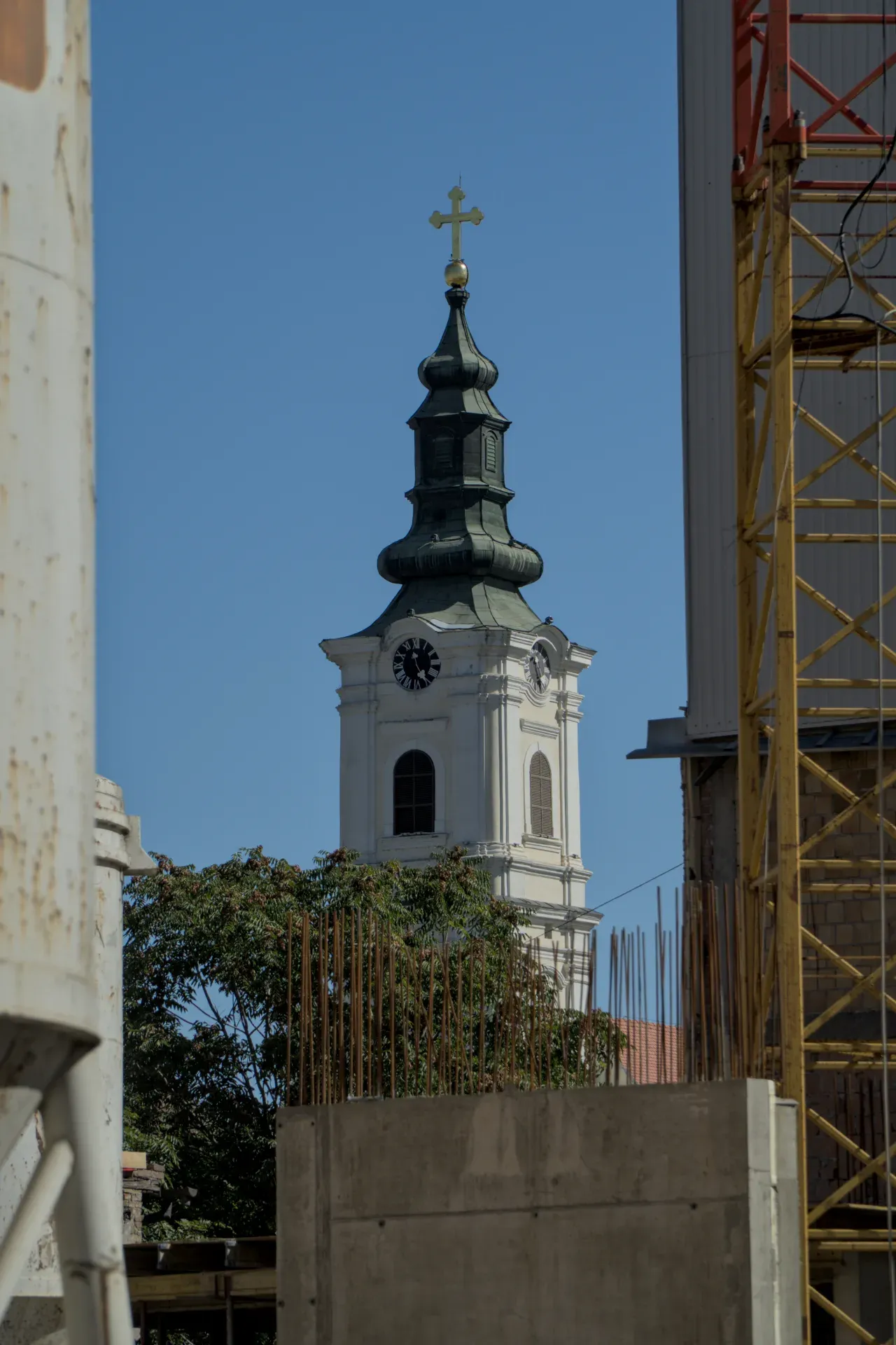 Der Kirchturm der Mariä-Entschlafens-Kirche in Novi Sad ragt mit seinem grünen Dach und goldenen Kreuz gegen einen klaren blauen Himmel auf.