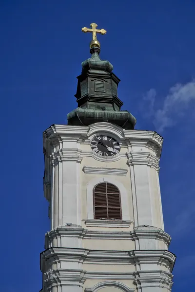 Bell tower of the Cathedral of the Assumption of the Holy Virgin Mary in Novi Sad with a golden spire and clock, under a blue sky.