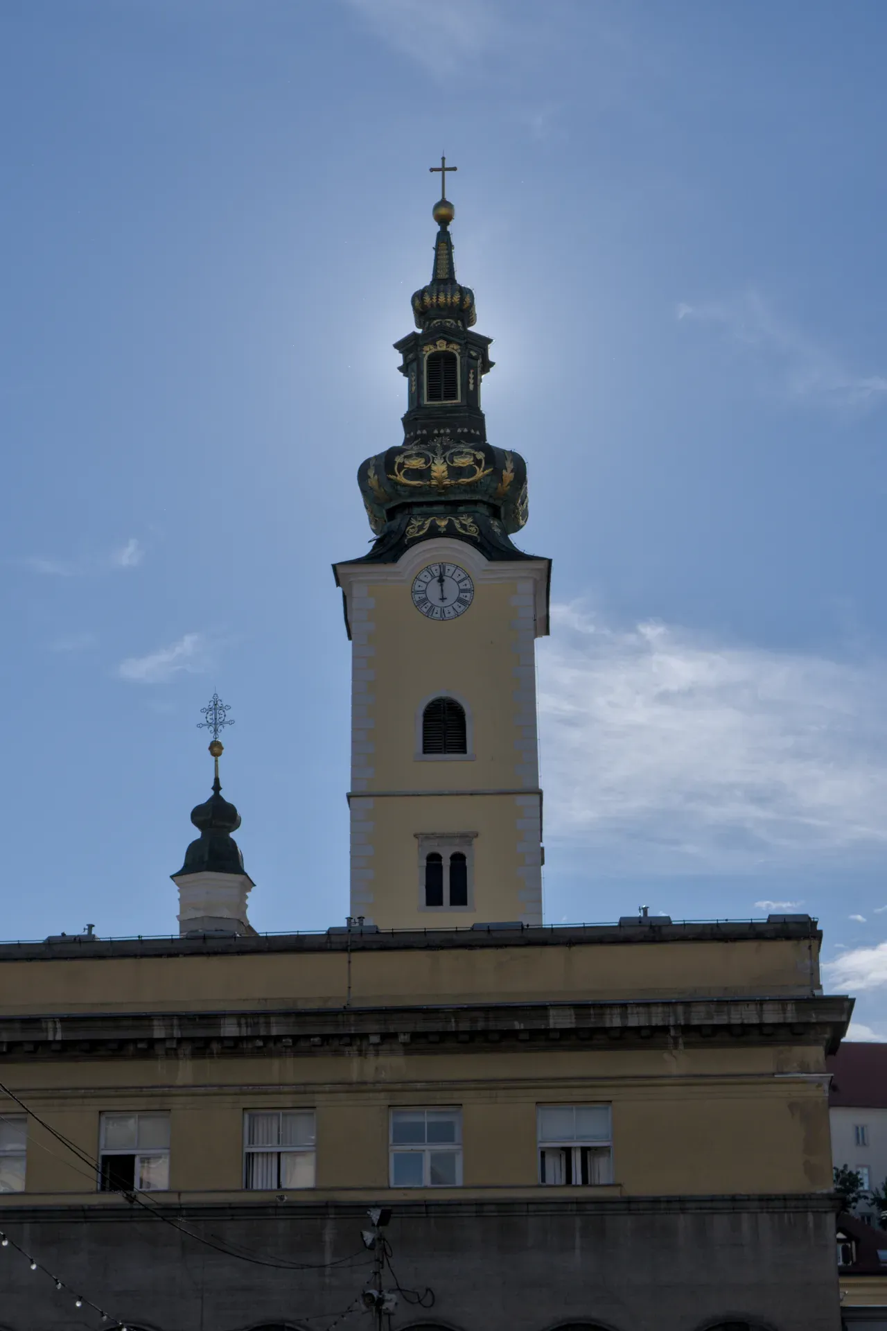 Ein vertikales Foto eines historischen Turms mit einer goldenen Kuppel und einer Uhr in Zagreb, Kroatien, gegen einen blauen Himmel.