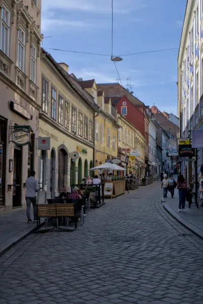 Eine belebte Gasse in Zagreb mit Cafétischen und traditioneller Architektur unter blauem Himmel.