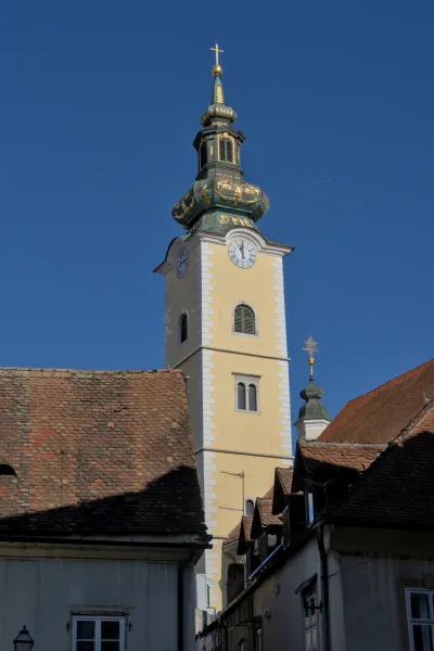 Ein detailreicher Kirchturm mit Uhr und kunstvollen goldenen Verzierungen, vor einem strahlend blauen Himmel, aufgenommen in Zagreb.