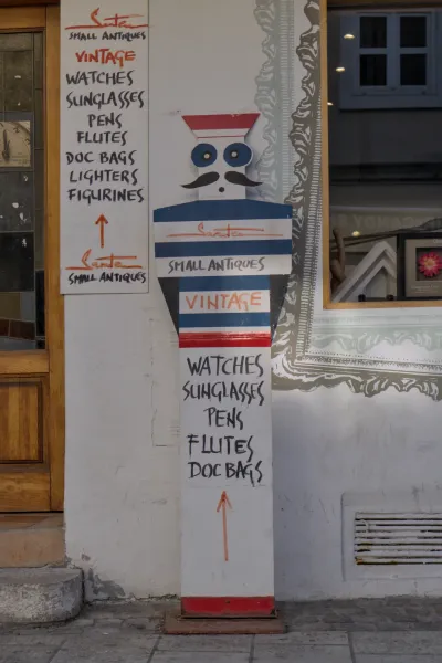 Ein handgemaltes Schild für ein Antiquitätengeschäft in Zagreb, das Vintage-Uhren, Sonnenbrillen und andere Artikel auflistet.