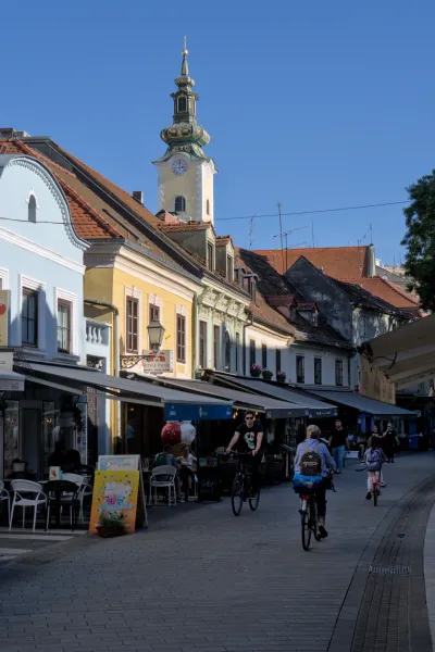 Ein charmantes Bild der Gasse in Zagreb mit einem markanten Kirchturm, der im Sonnenlicht strahlt.