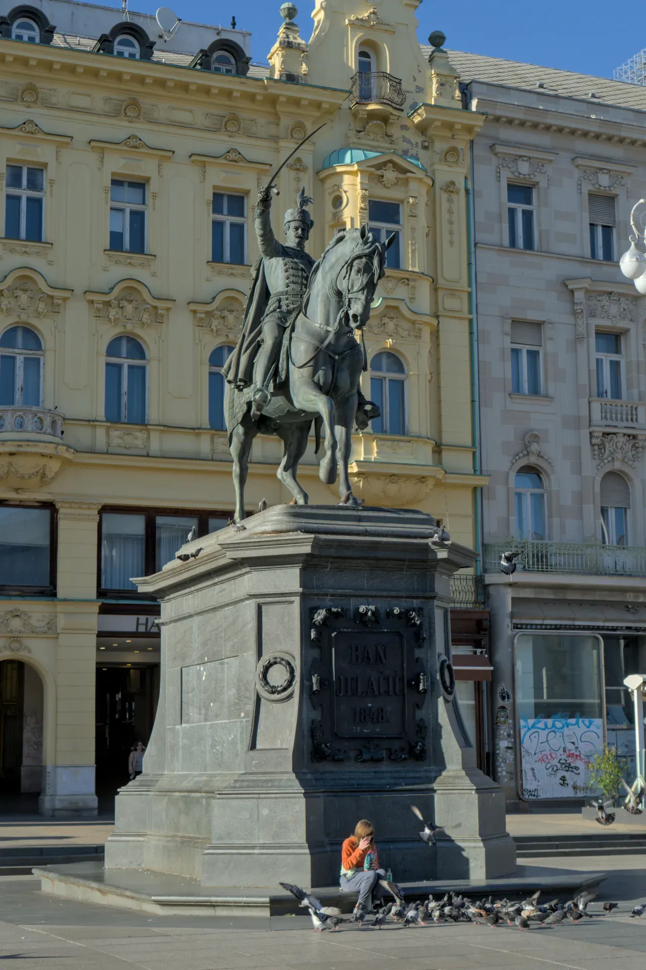 The equestrian monument of Ban Jelačić in Zagreb, Croatia, with a person feeding pigeons.