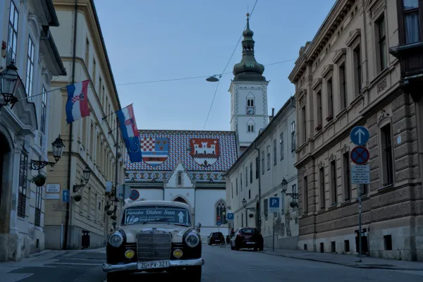 Klassisches Auto und St. Markus Kirche in Zagreb mit kroatischen Flaggen im Abendlicht.