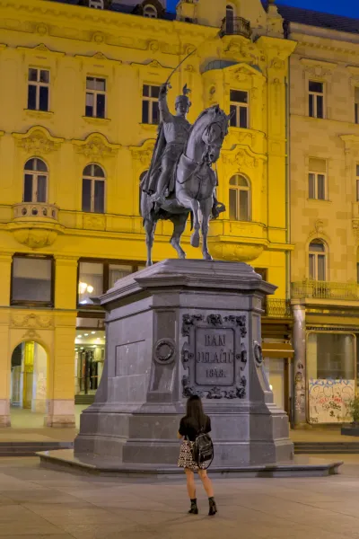Ban Jelačić Denkmal bei Nacht mit Reiterstatue und einer Person, die es betrachtet.