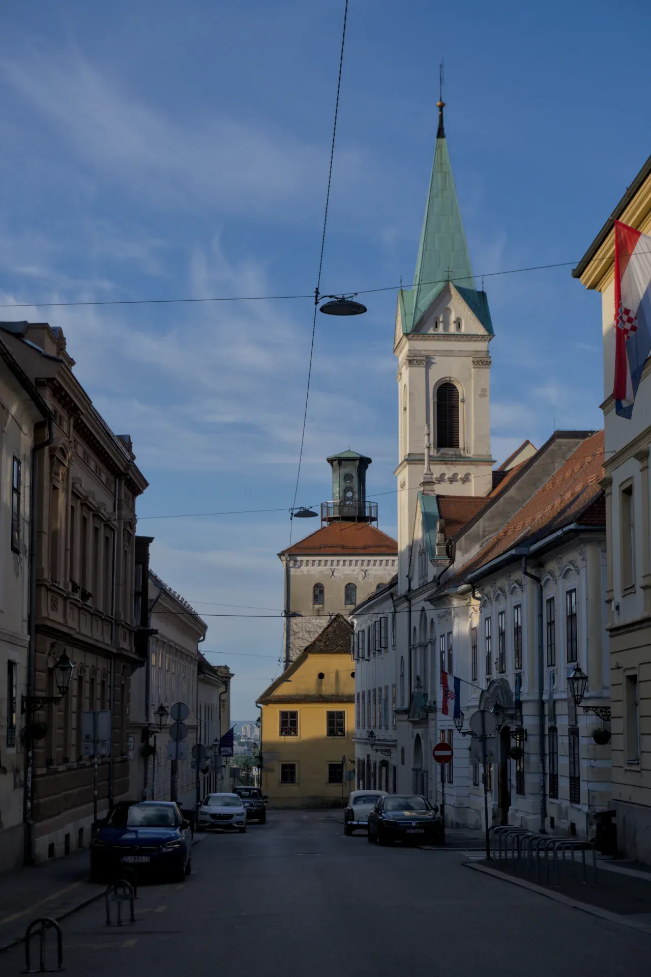 View into a narrow alley in Zagreb with historic buildings and a prominent church tower in the background.