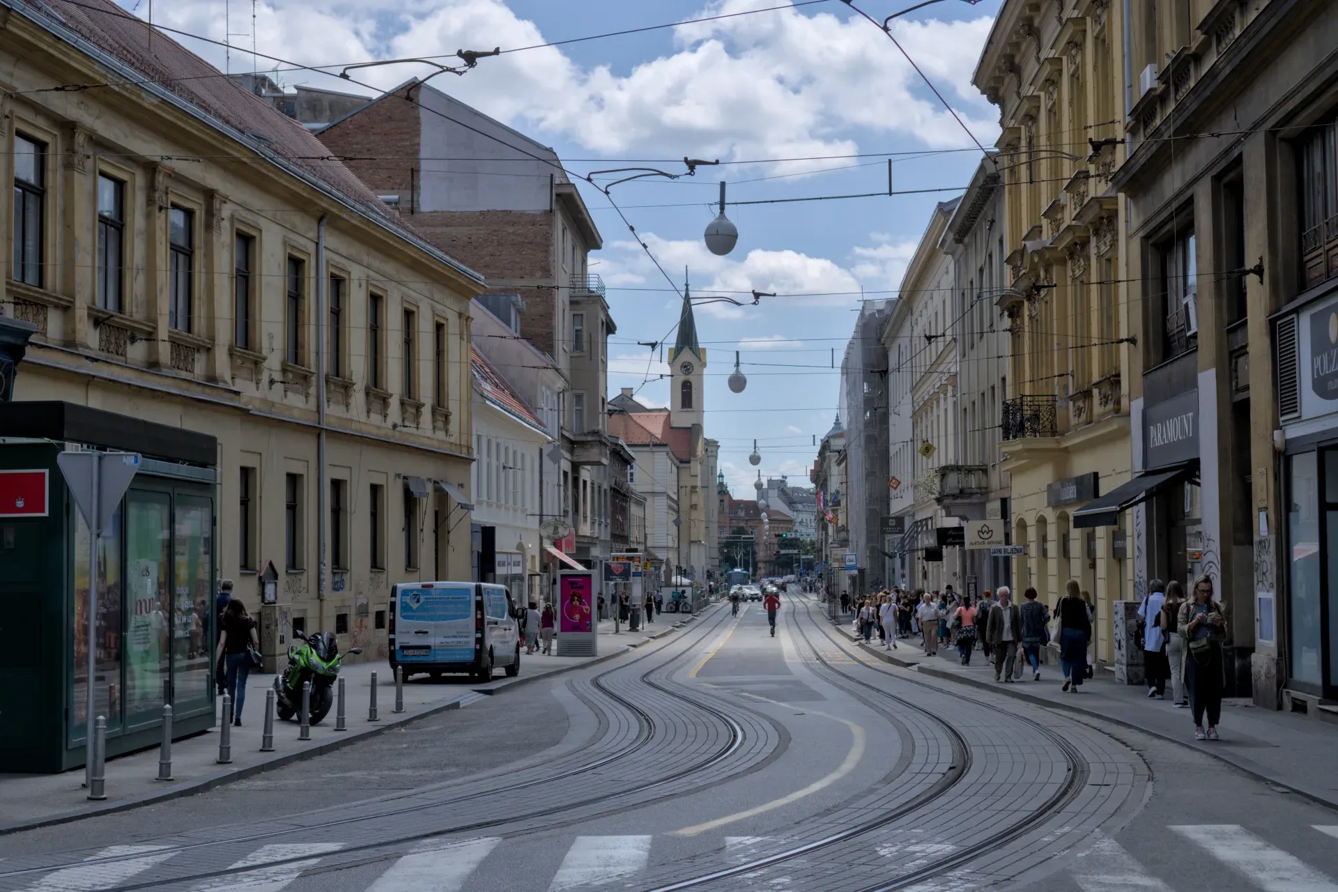 A dynamic shot of a street in Zagreb, Croatia, with winding tram tracks and historic buildings illuminated by a cloudy sky.