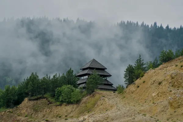 Pagoda-like house on a hill above Zaovine Lake in Tara National Park, surrounded by pine trees and fog.