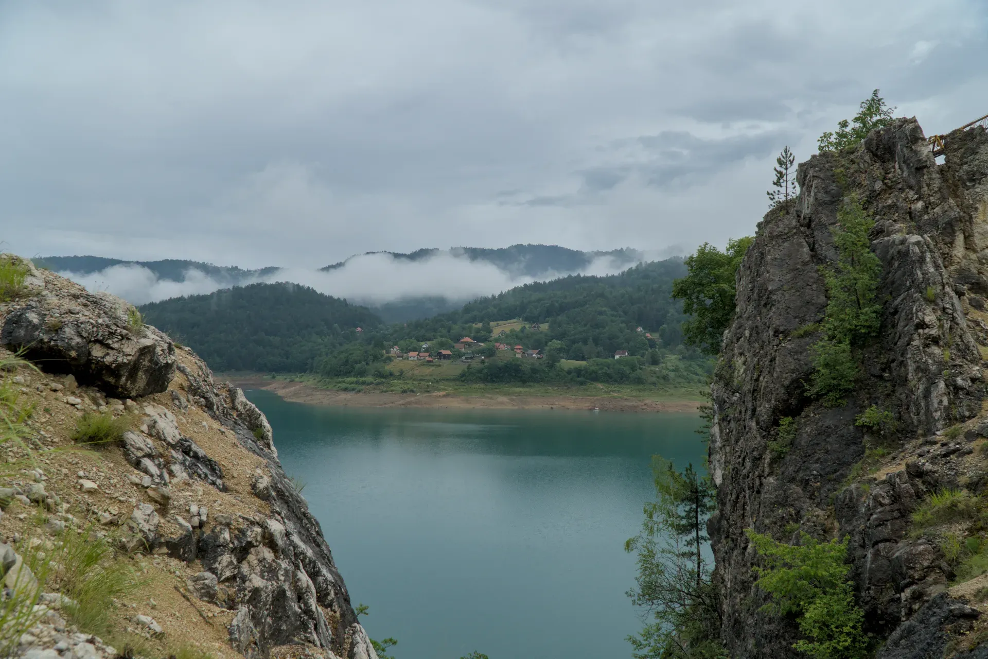 Panorama of Zaovine Lake between rugged rocks, with forested hills and mist in the background.