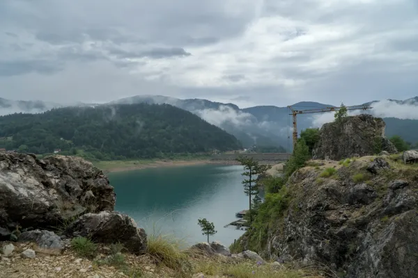 Rugged landscape at Zaovine Lake with fog and clouds, framed by rocks, trees, and mountains.