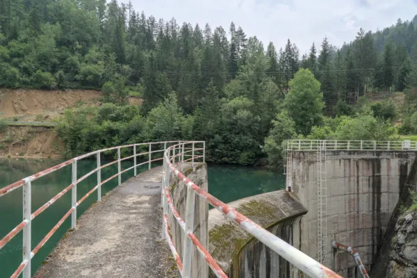 A path with a railing leads to a concrete structure, the Spaiic Lake Dam, in Tara National Park Serbia, surrounded by green forest.
