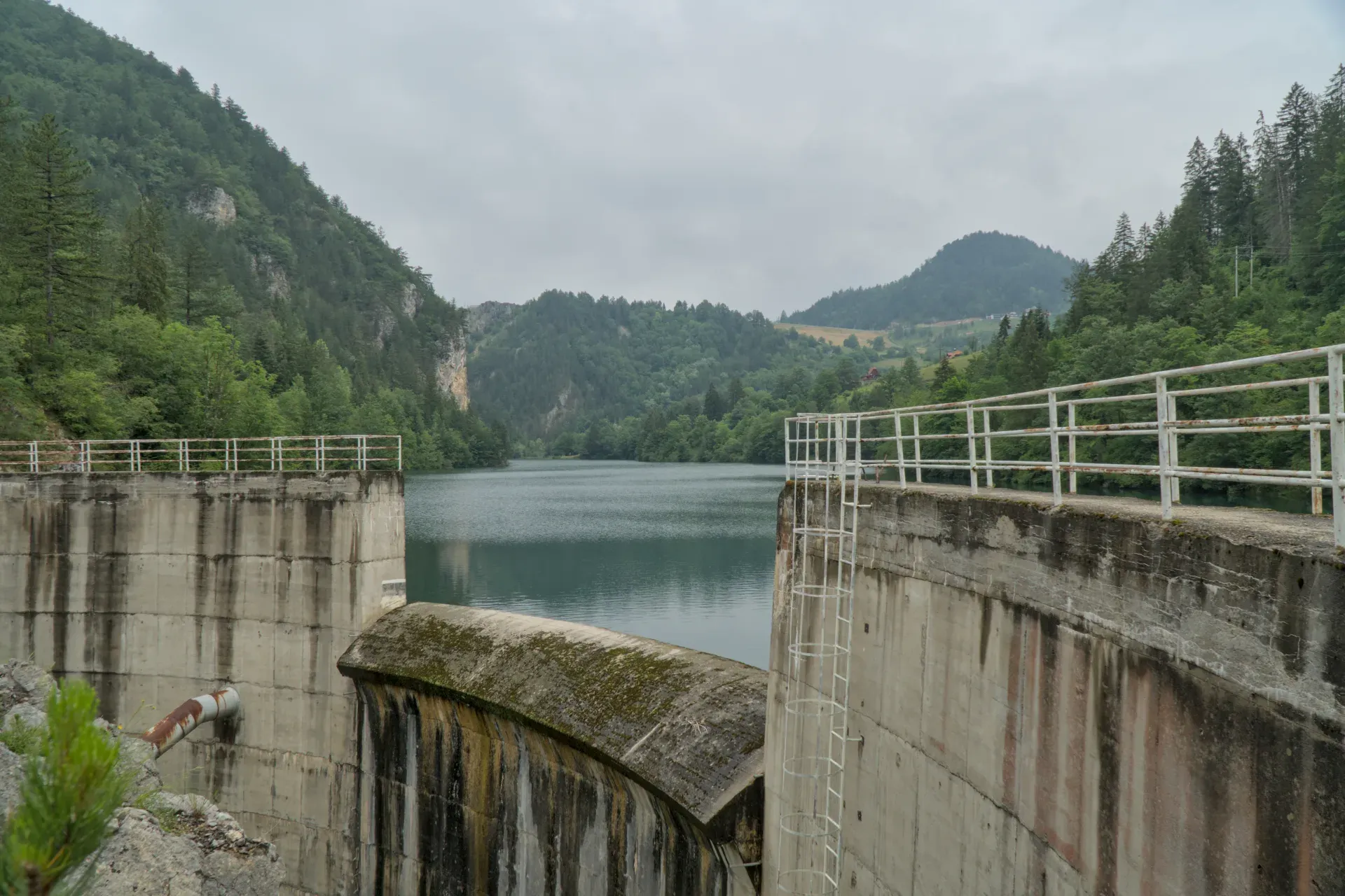 La diga sul Lago Spajića in Serbia, circondata da montagne boscose, con acqua calma.
