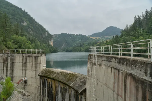 The dam at Spajića Lake in Serbia, surrounded by forested mountains, with calm water.
