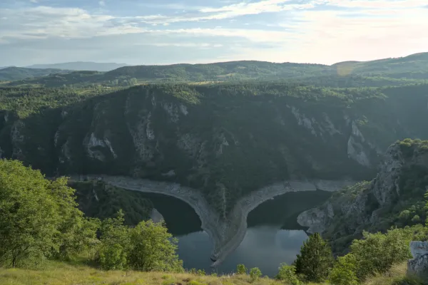 The Uvac Canyon in Serbia with its distinctive river bend at sunset, surrounded by forested hills.