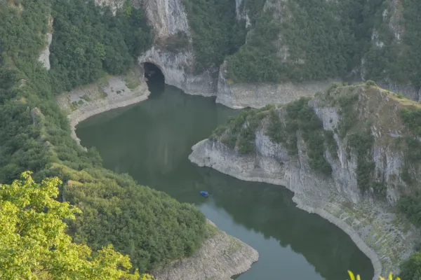 The Uvac Canyon in Serbia showcases winding river bends and the Ušačka Cave, with a small blue boat in the water.
