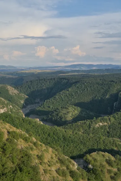 A winding canyon in Serbia, illuminated by the soft light of sunset, with green hills and a river.