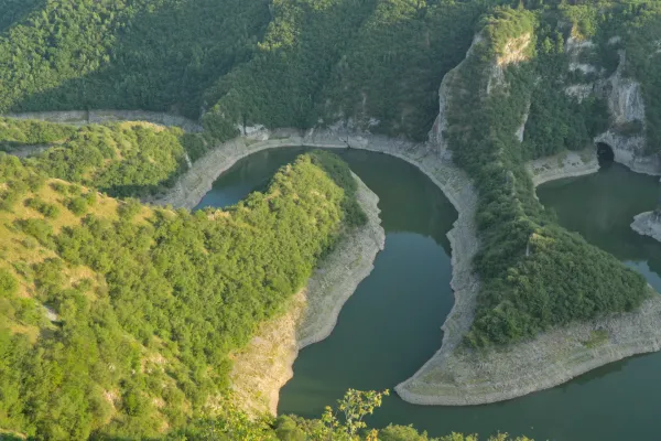 A winding riverbed under the setting sun, surrounded by green hills in Serbia.
