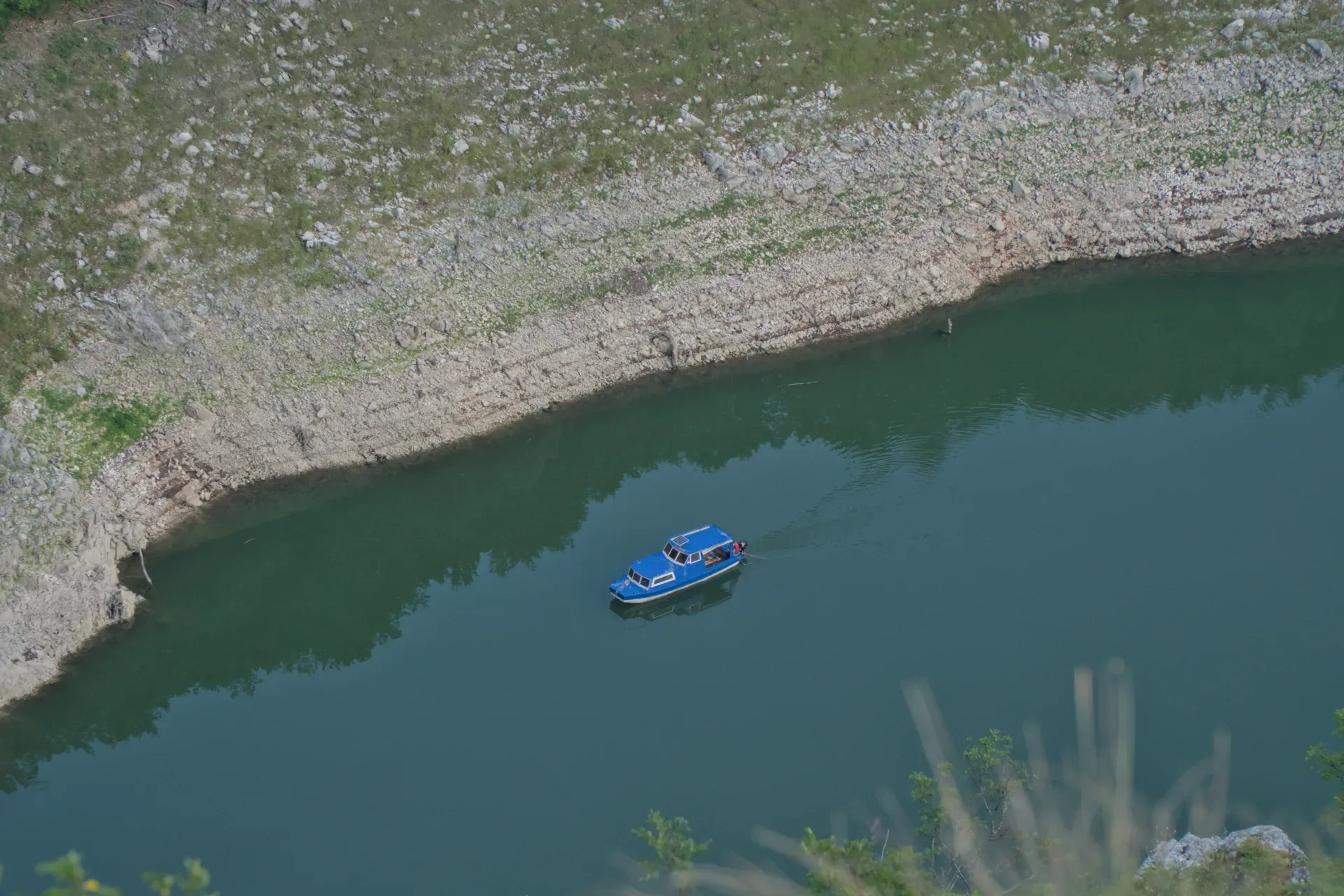 Un bateau d'excursion bleu navigue dans les gorges de l'Uvac, entouré de rives rocheuses et d'eau verte profonde.