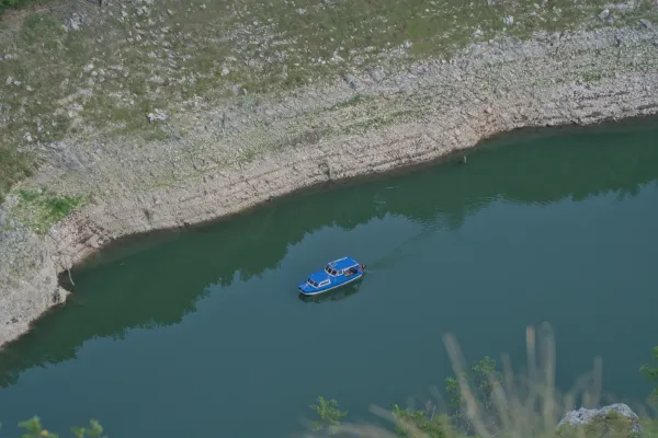 A blue excursion boat travels through the Uvac Gorge, surrounded by rocky banks and deep green water.