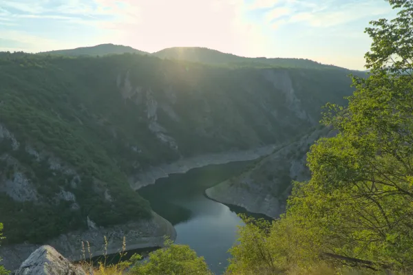 Meanders of the Uvac River at sunset, surrounded by green hills and rugged cliffs.