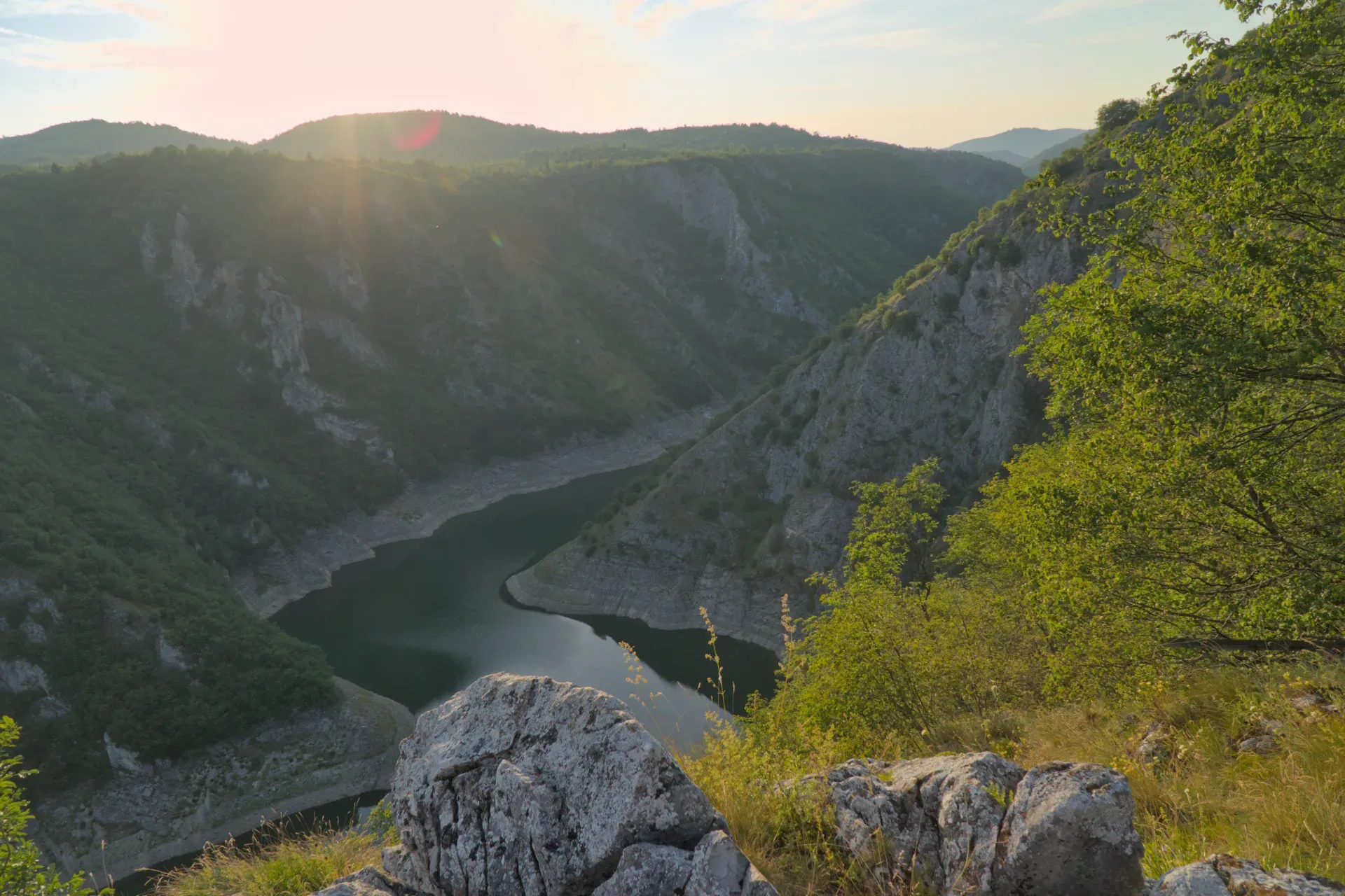 Scenic view of the Uvac Canyon in Serbia, with a river winding through forested slopes, illuminated by warm evening light.