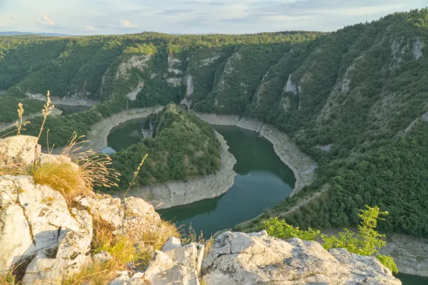 The Uvac river bend in Serbia at sunset with lush vegetation and rocky shores.