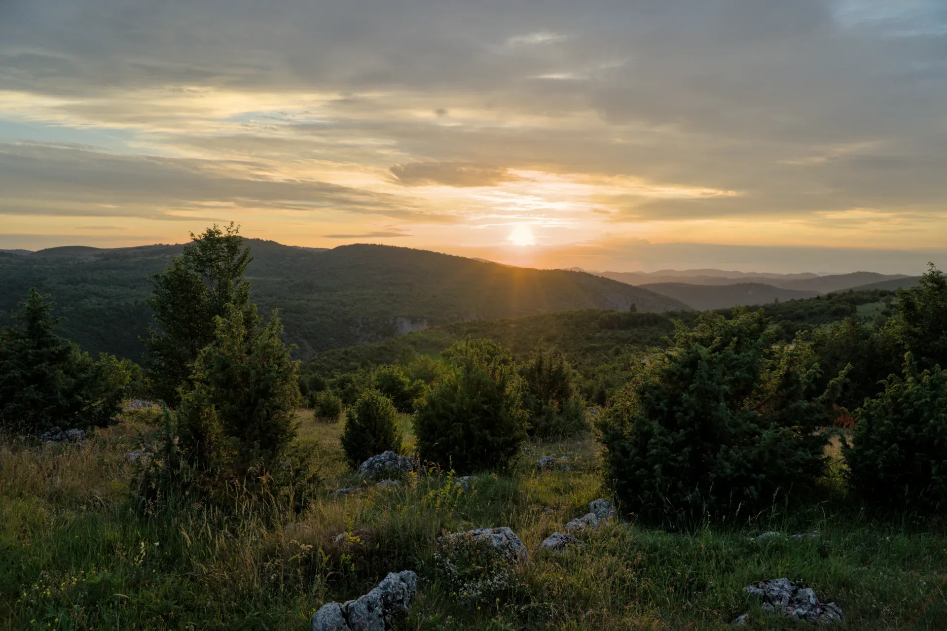 Sunset over the Uvac Valley from Mljetva Viewpoint, Serbia, with dramatic clouds and sun-drenched hills.
