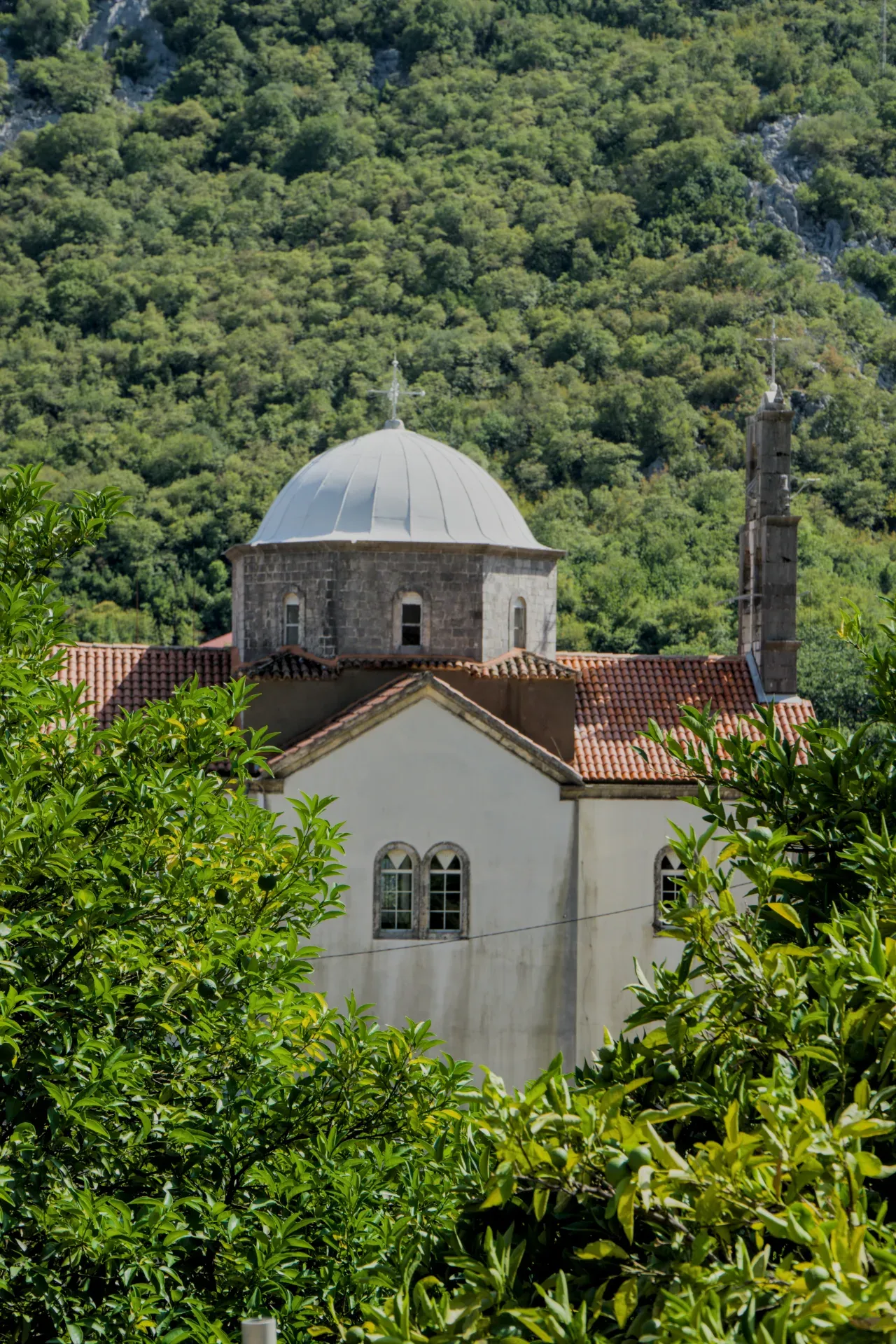 Una iglesia en una montaña en Morinj, Montenegro, rodeada de denso follaje verde.