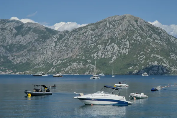 Various boats and yachts floating in the water with a mountainous backdrop in Kotor Bay.